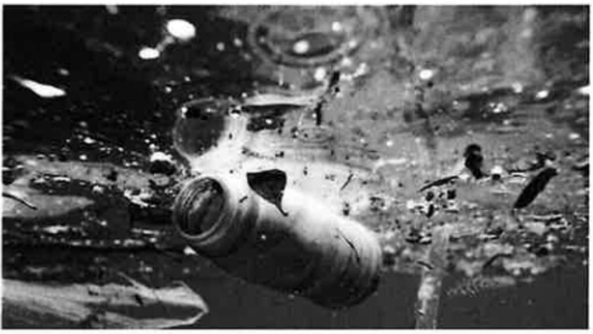 A photograph of a bottle under polluted water.